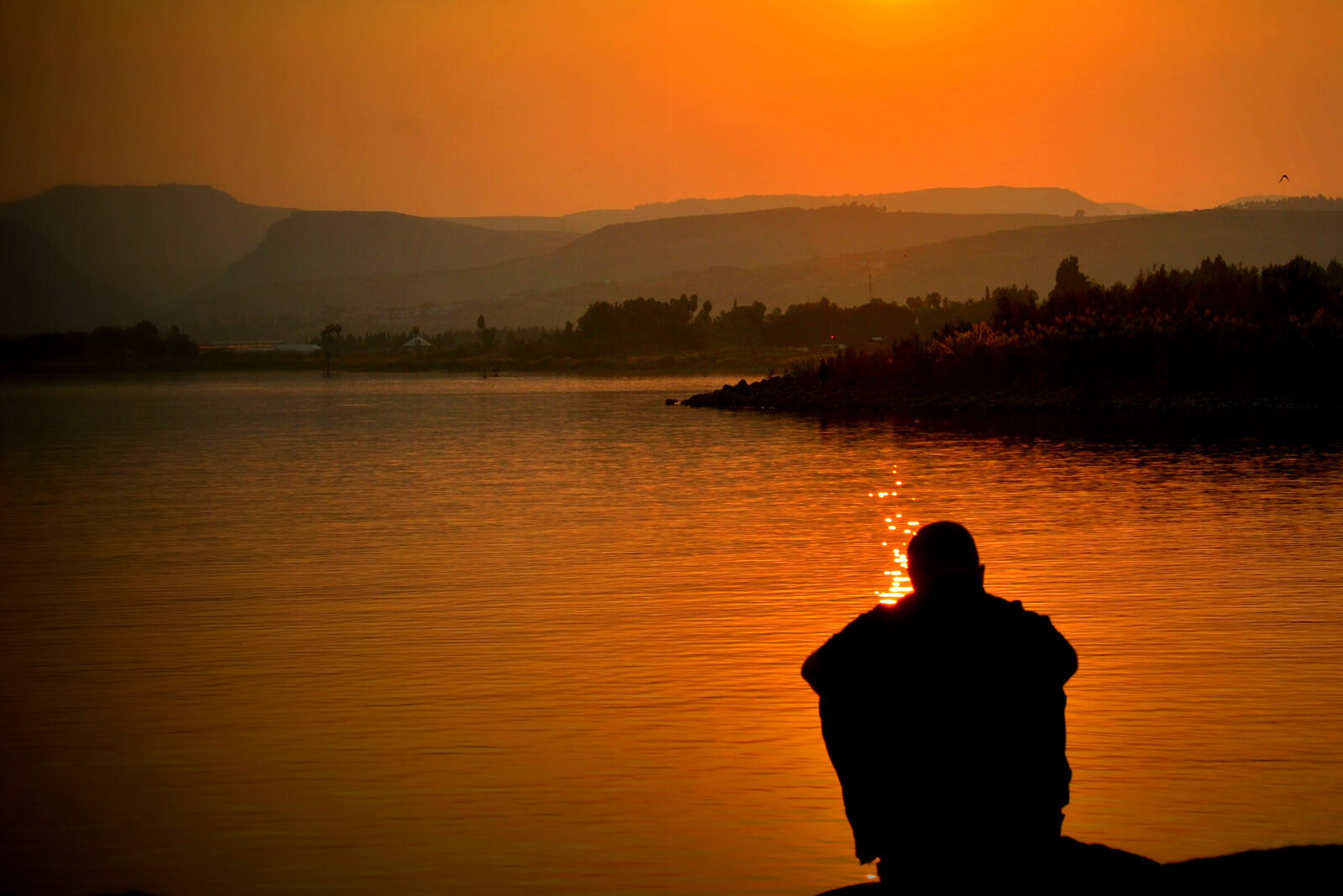 Mann sitzend am Ufer während eines Sonnenuntergangs